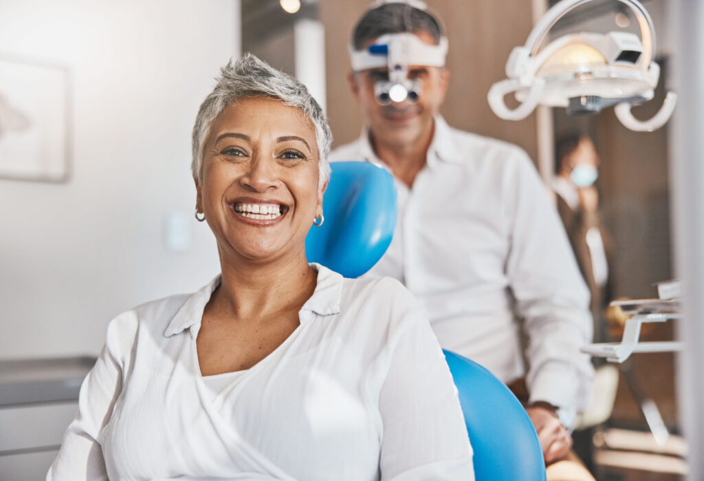 Woman sitting in the oral surgery chair smiling at the camera--the surgeon is in the background